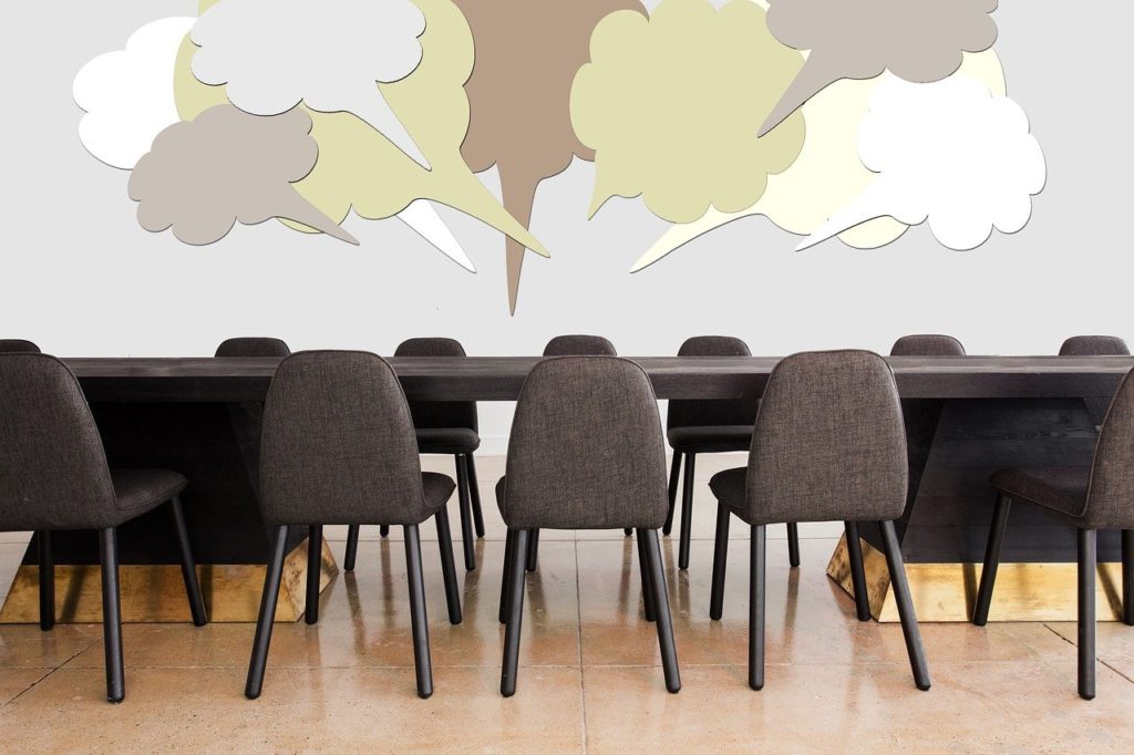 Empty chairs around a conference table, ideas and speech bubbles rise up from the chairs