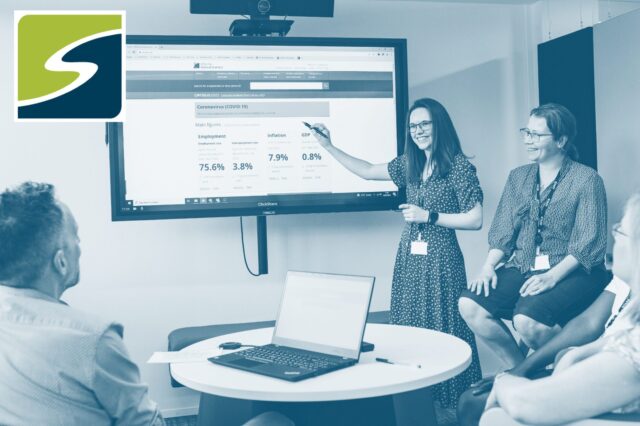 People stood around a screen smiling and talking